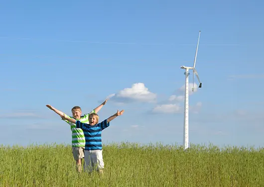 2 young boys in a meadow with a wind turbine in the background